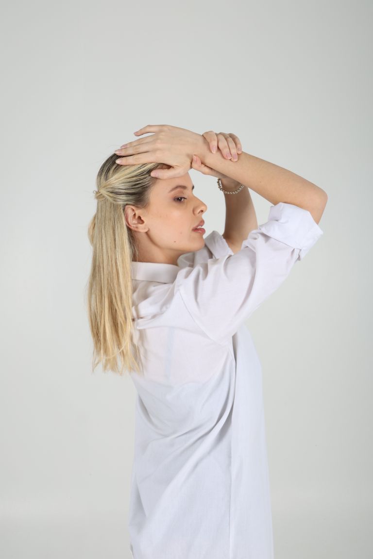 Martina de perfil con camisa blanca y las manos sobre la cabeza.