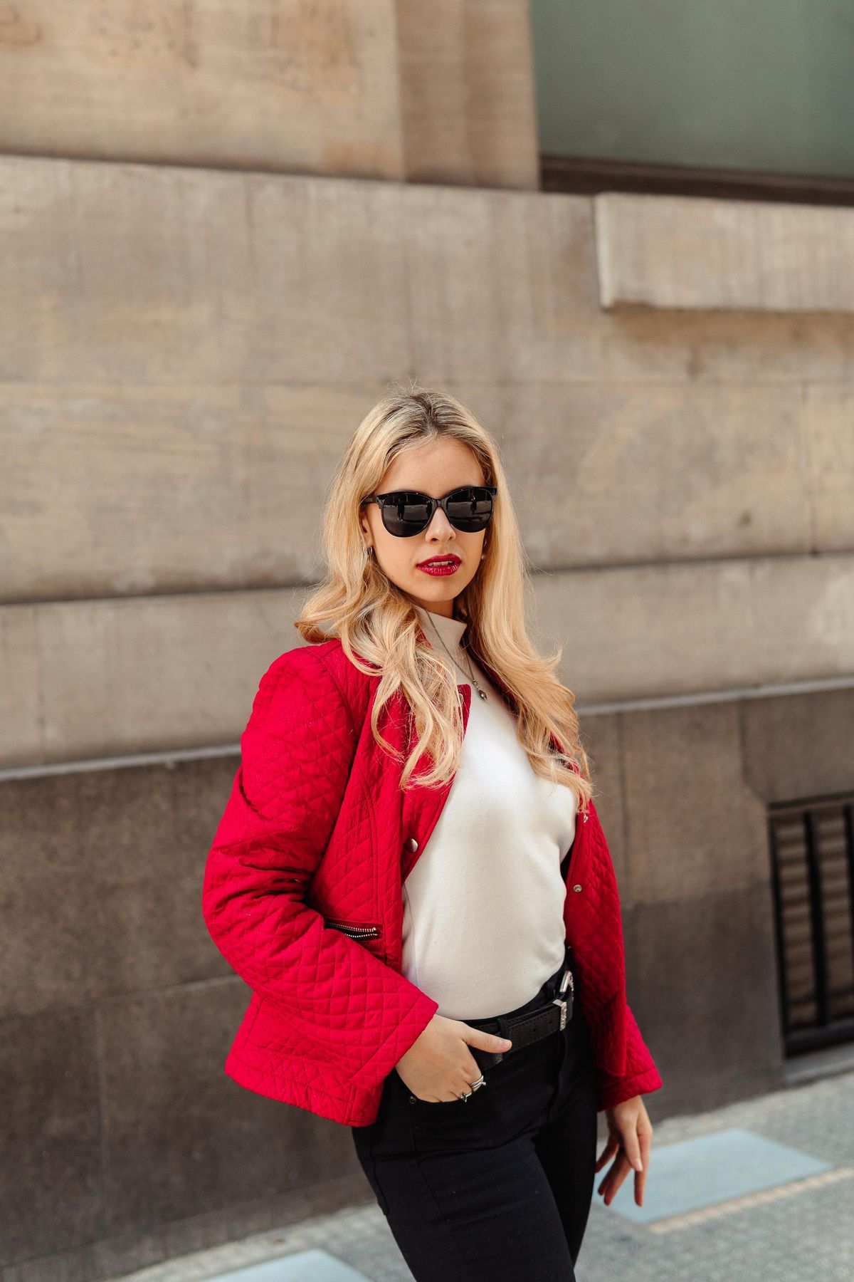 Martina con chaqueta roja y gafas oscuras junto a un muro.