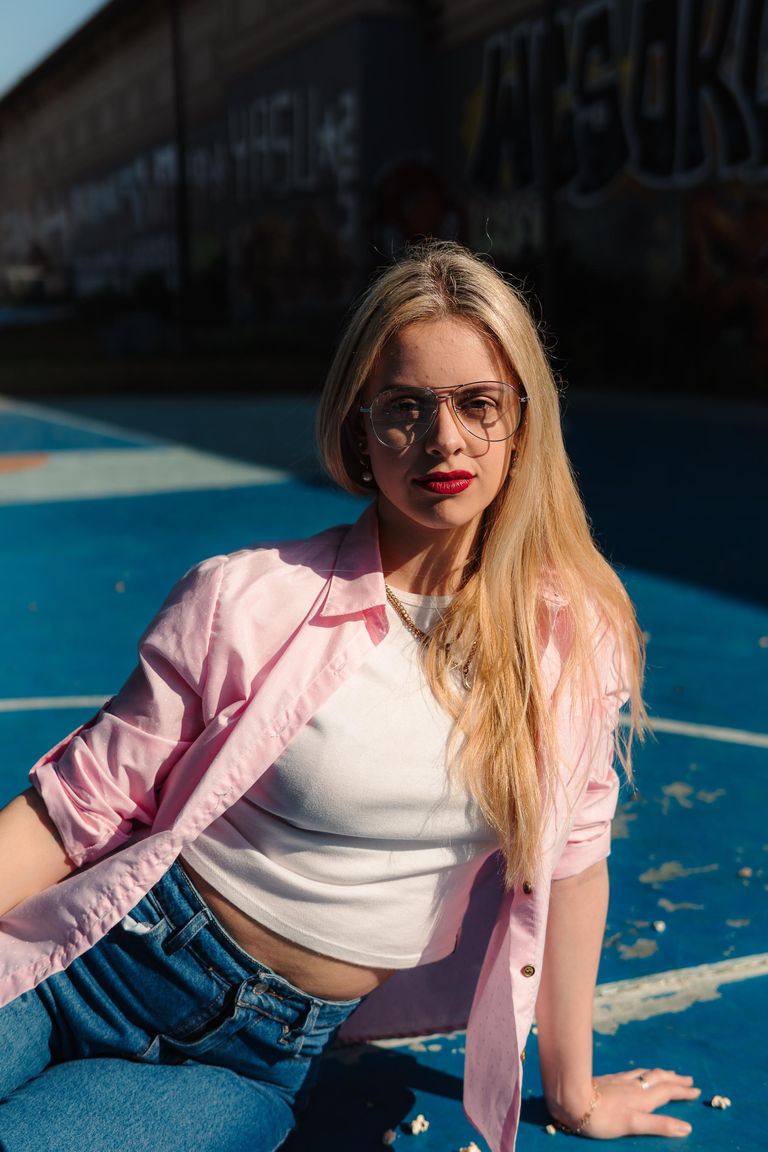Martina sentada con chaqueta rosa y gafas bajo luz intensa.