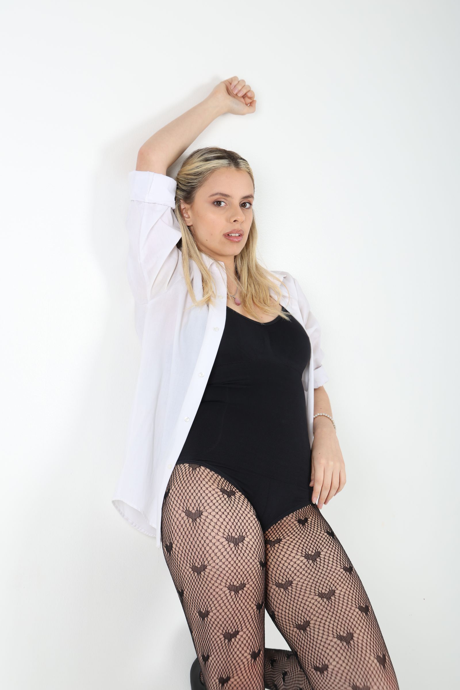 Martina posa con camisa blanca abierta y una mano sobre la cabeza.