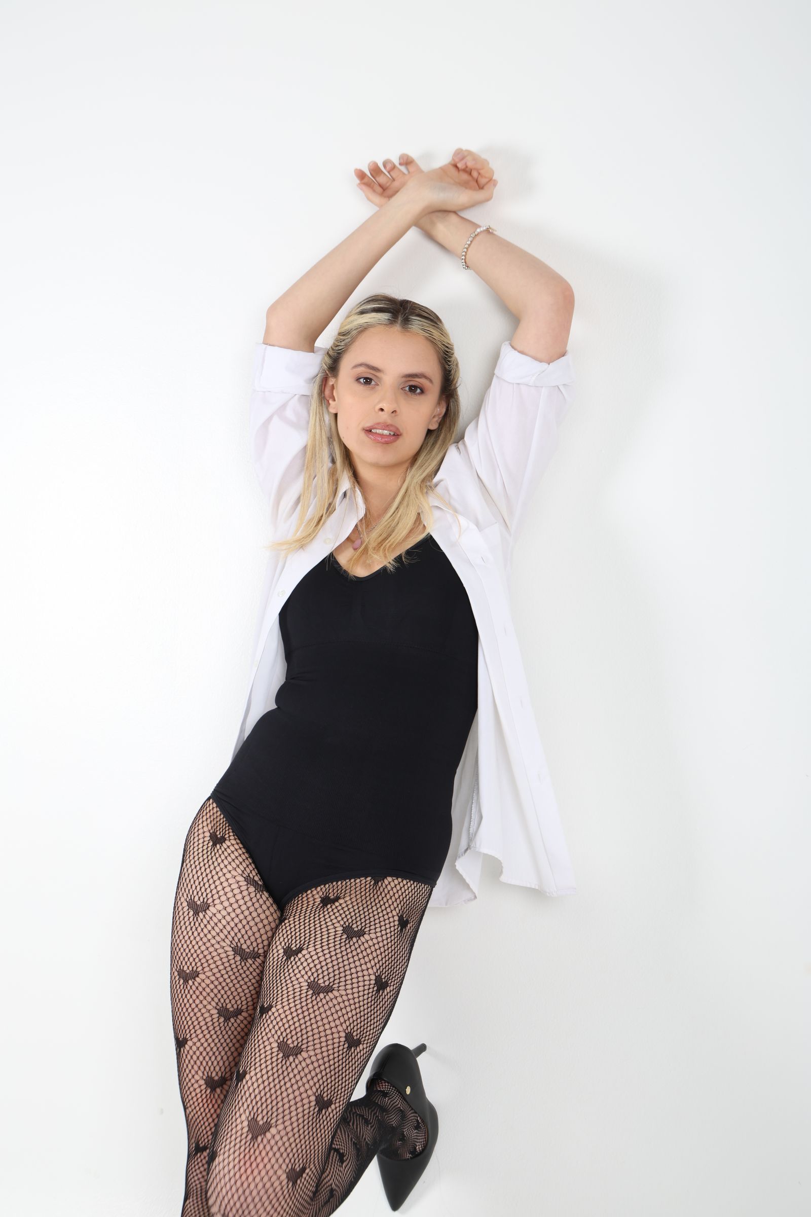 Martina con camisa blanca y ambos brazos elevados sobre fondo claro.