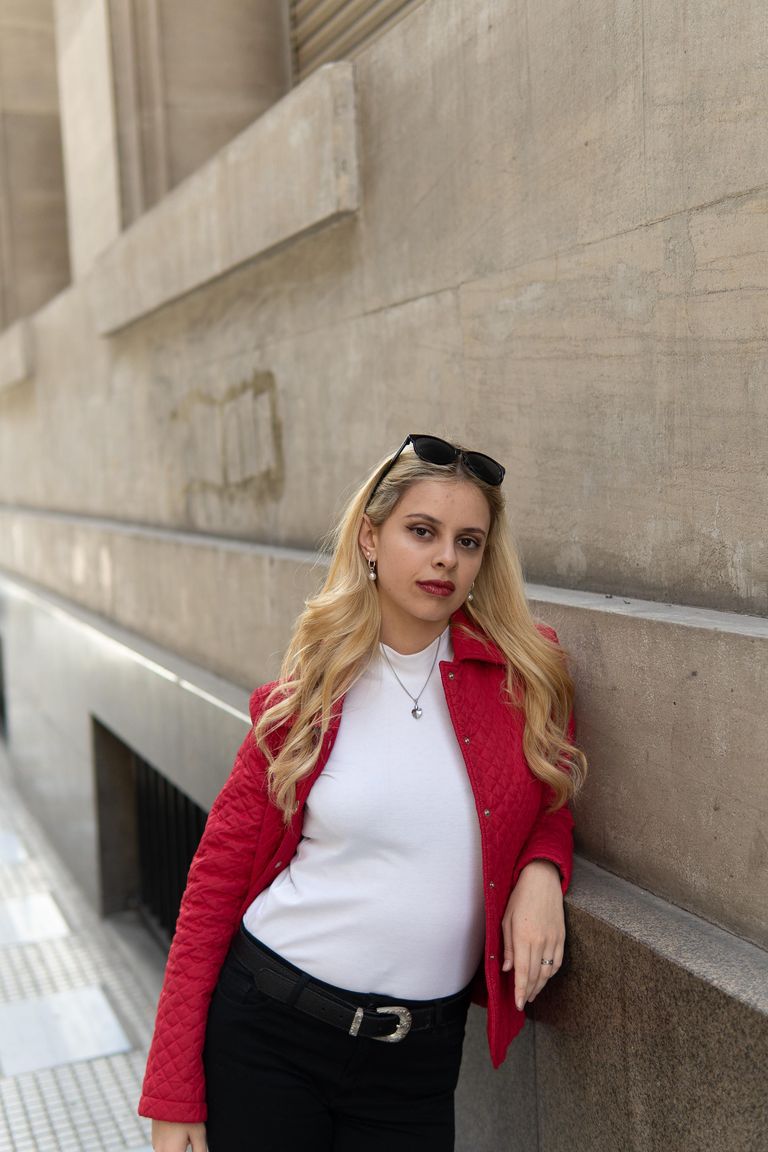 Martina con chaqueta roja, apoyada en una pared de piedra.