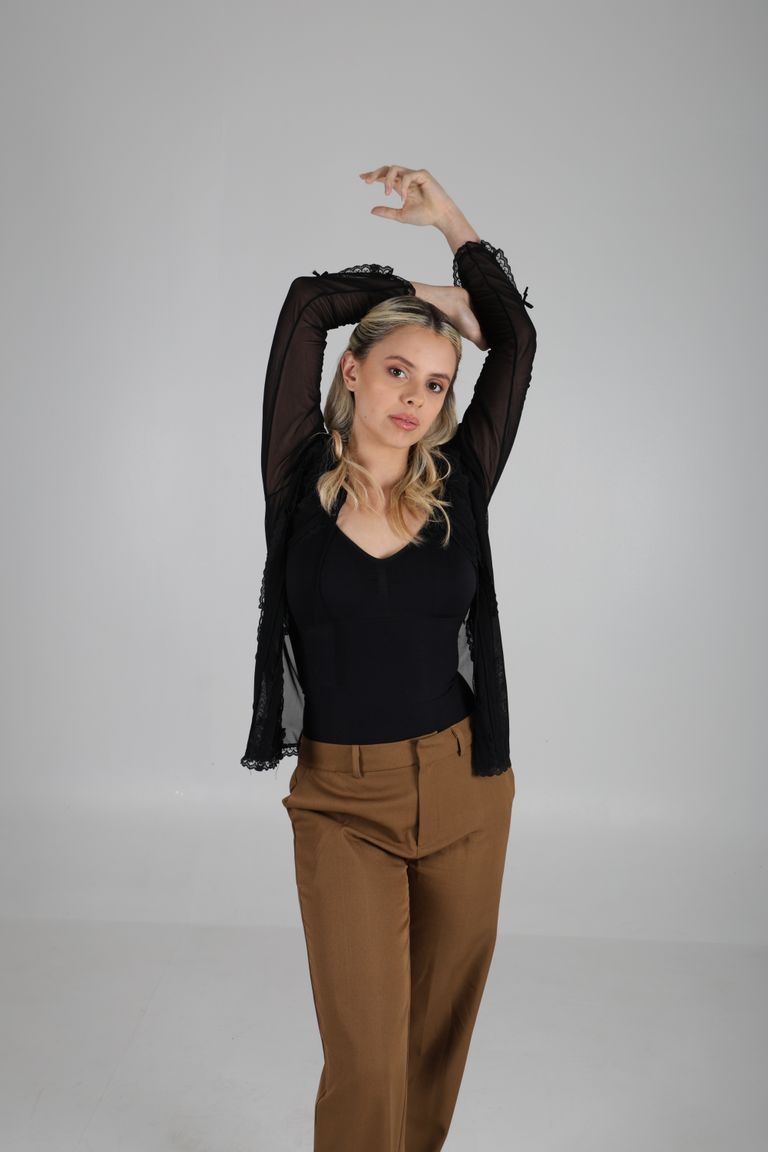 Martina de cuerpo entero con blusa negra y un brazo elevado.