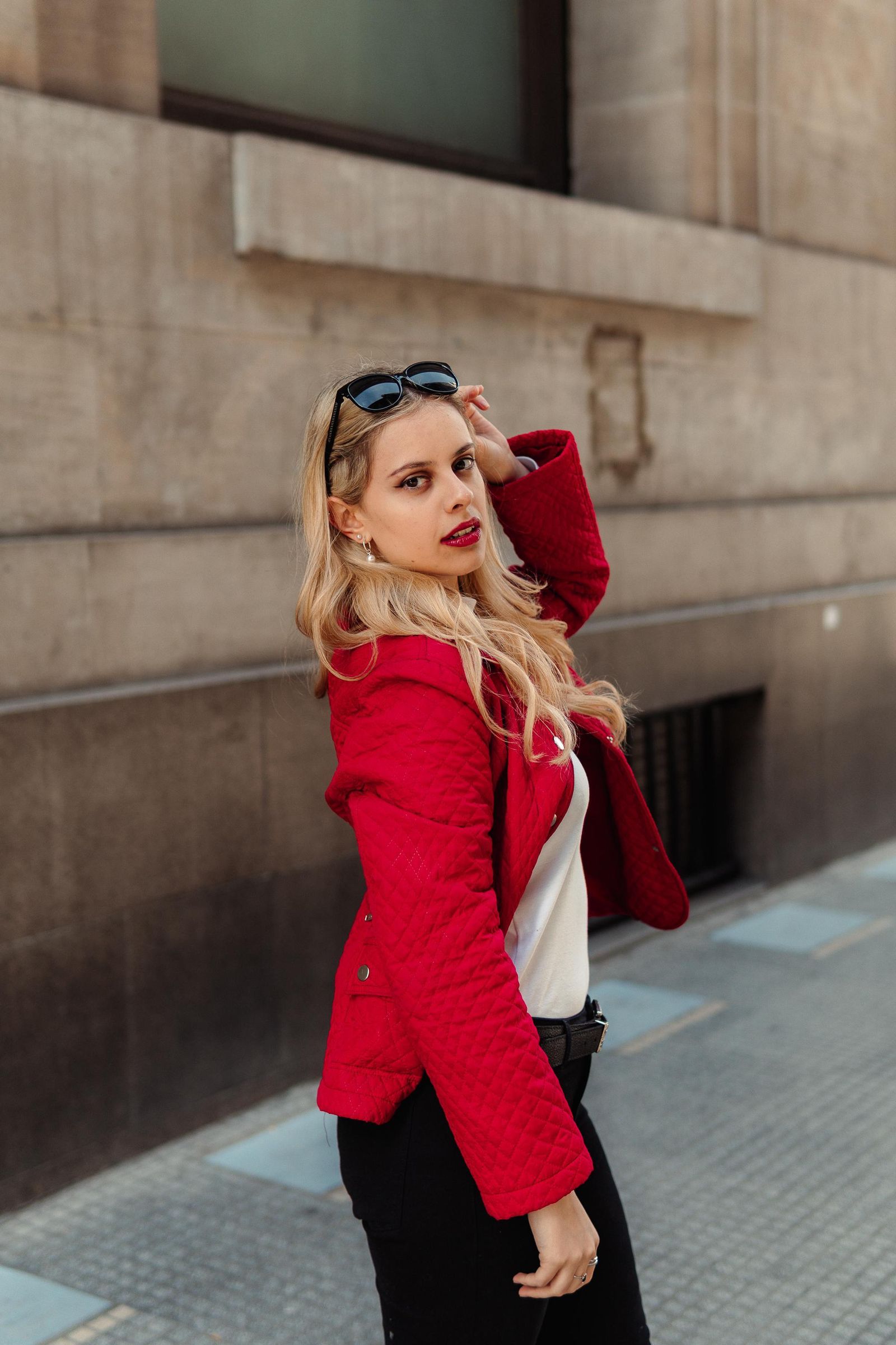 Martina con chaqueta roja posa de perfil junto a un edificio.