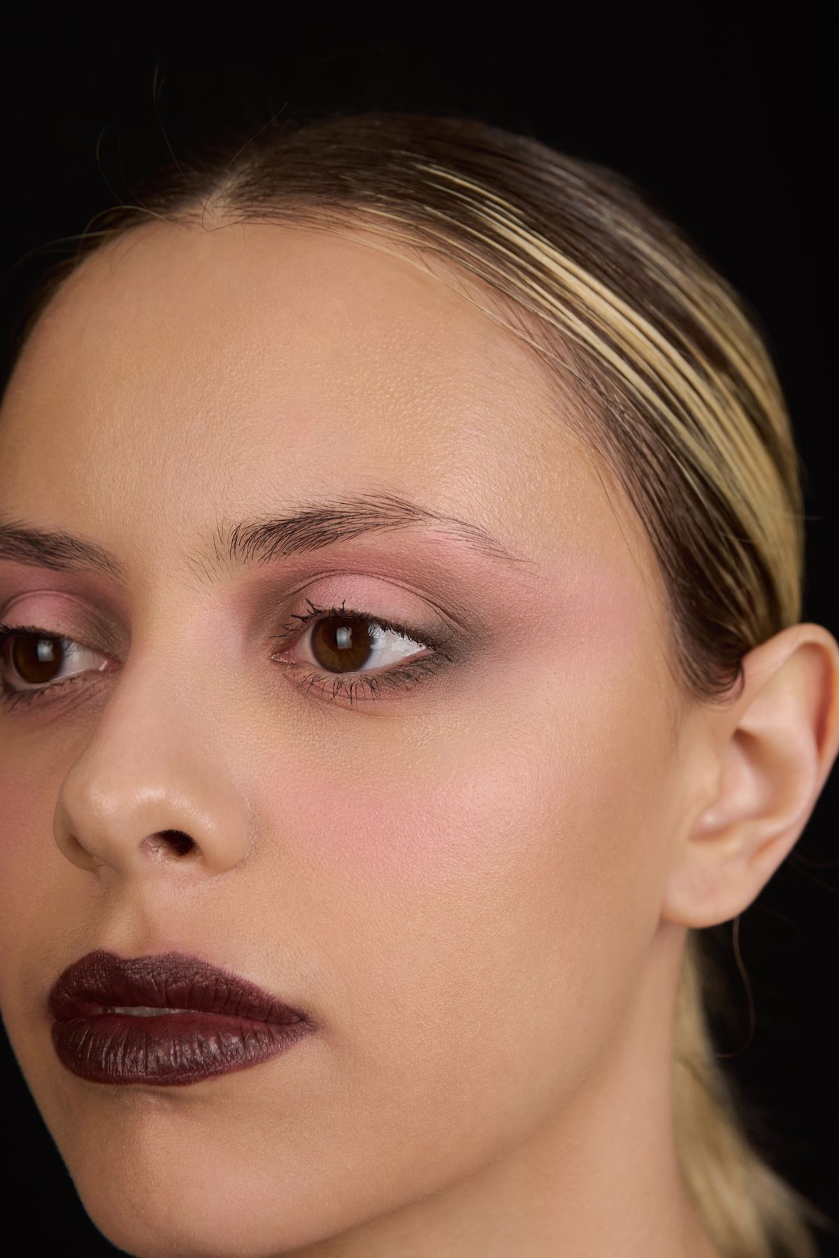 Retrato cercano de Martina con maquillaje oscuro sobre fondo negro.