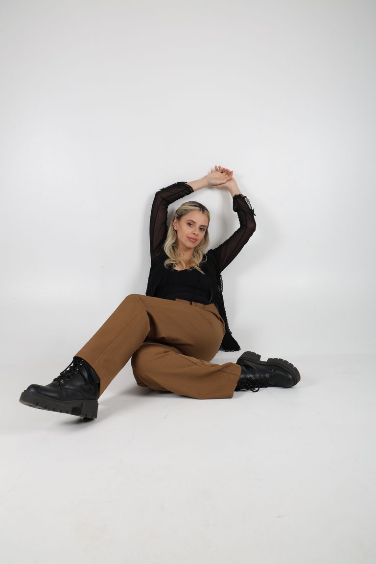 Martina sentada sobre fondo claro con blusa negra y pantalón camel.