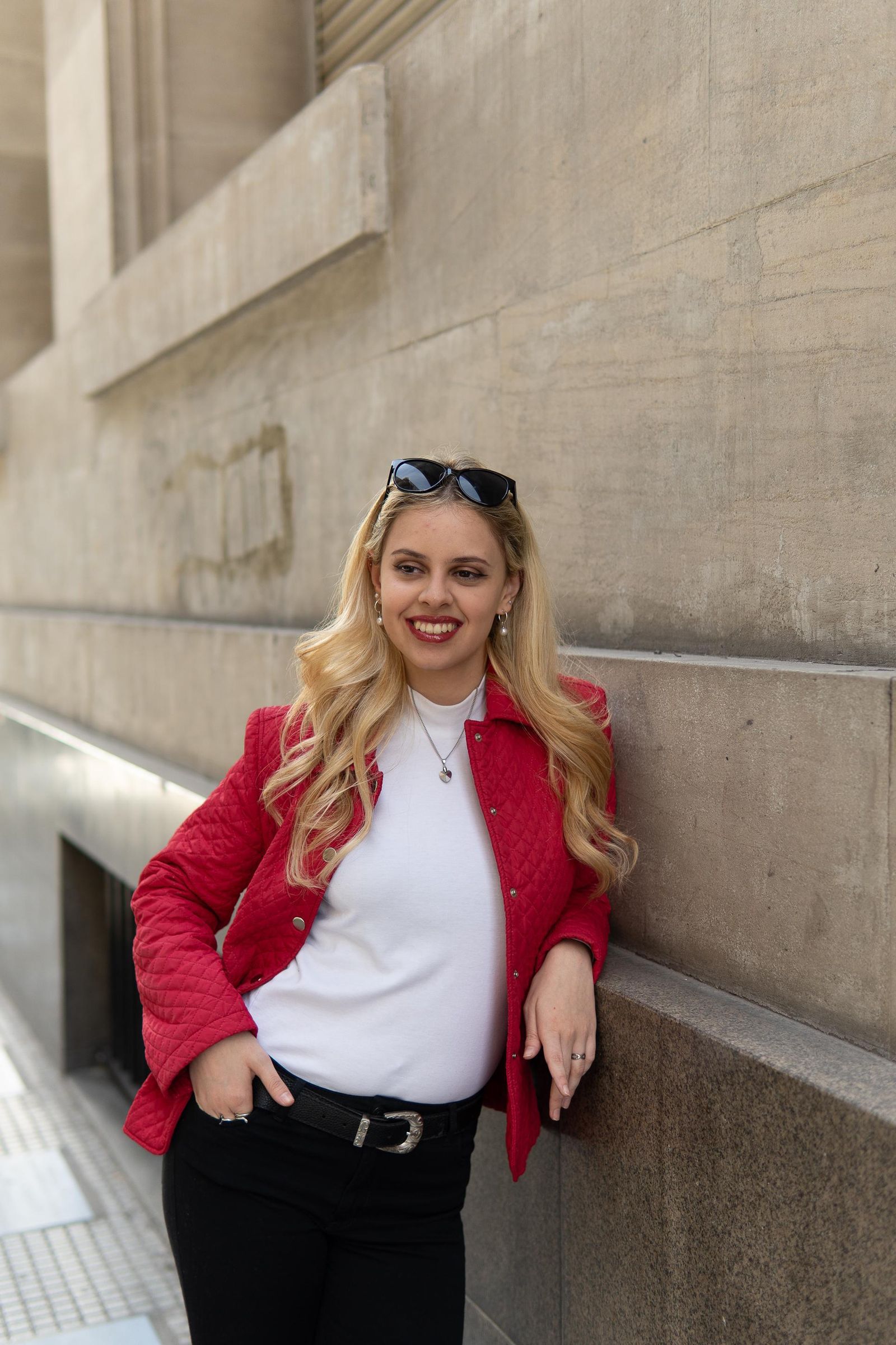 Martina con chaqueta roja, apoyada en un muro de piedra y sonriendo.