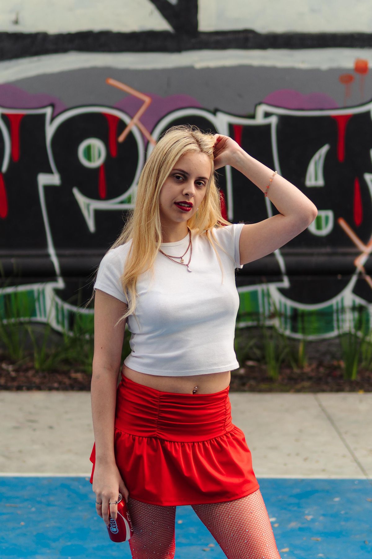 Martina con top blanco y falda roja frente a un muro con grafiti.